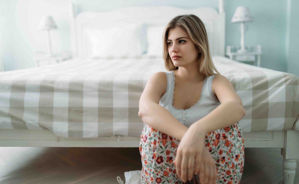 Depressed young woman sitting on bed at home